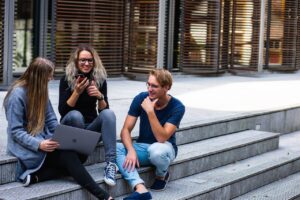 Three young professionals having a friendly chat while sitting on outdoor steps.