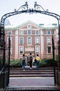 Three students walk through an archway towards a historic university building on campus.
